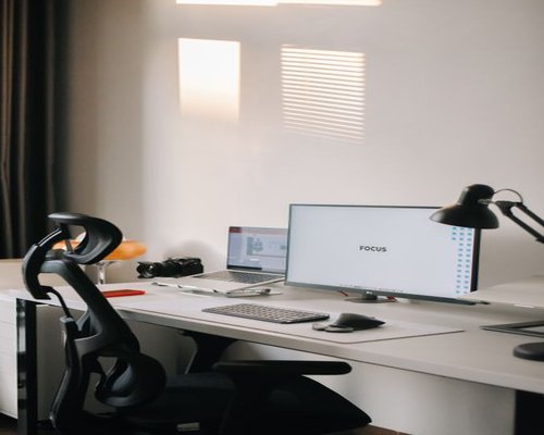 A well-lit clean minimalist workstation with an ergonomic chair and monitor at eye level